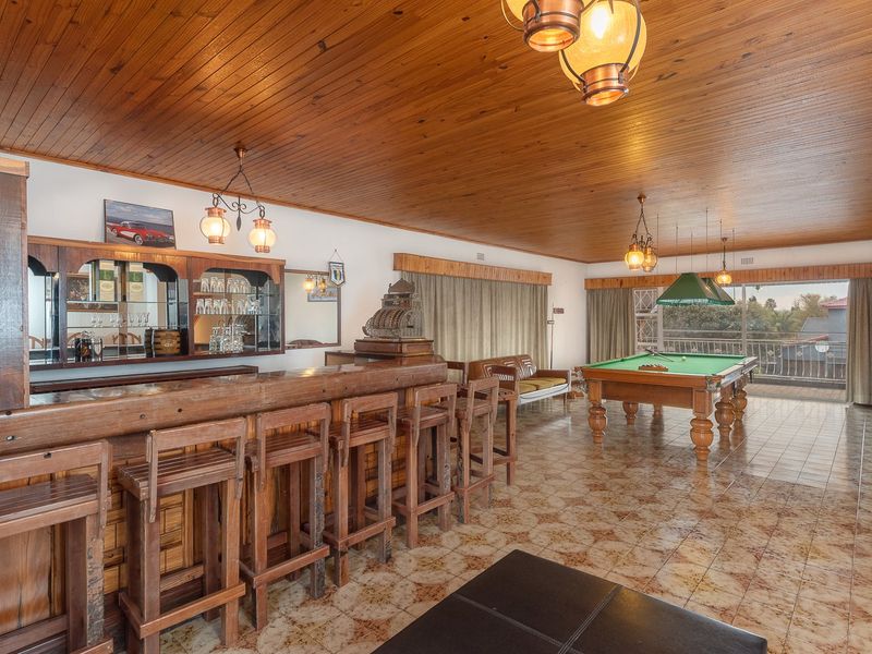 Spacious entertainment room featuring a built-in wooden bar, tiled flooring, wood-paneled ceiling, and direct access to an outdoor balcony through sliding glass doors.