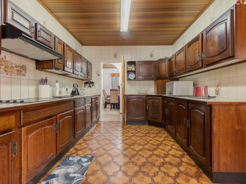 A traditional galley-style kitchen featuring extensive dark wood cabinetry, tiled backsplash, and a wooden ceiling, offering a classic layout with potential for modernization.