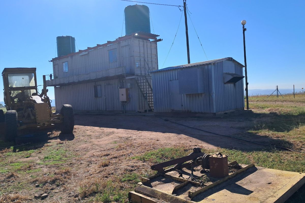 Exterior view of a utilitarian container-based structure featuring elevated water storage tanks and metal cladding on a rural small holding property.