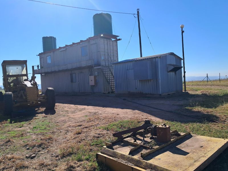 Exterior view of a utilitarian container-based structure featuring elevated water storage tanks and metal cladding on a rural small holding property.