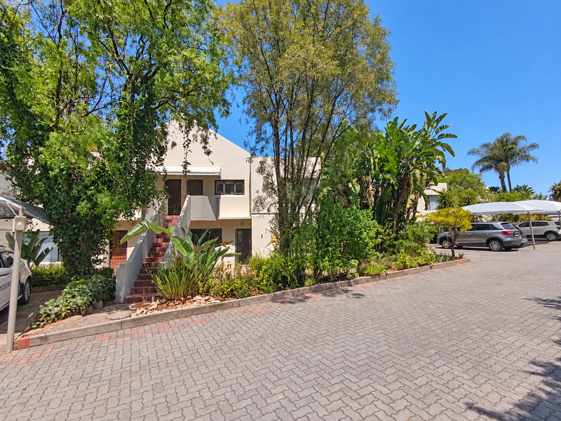 Exterior view of the apartment complex featuring a paved driveway, covered parking bays, and established garden landscaping leading to the building entrance.