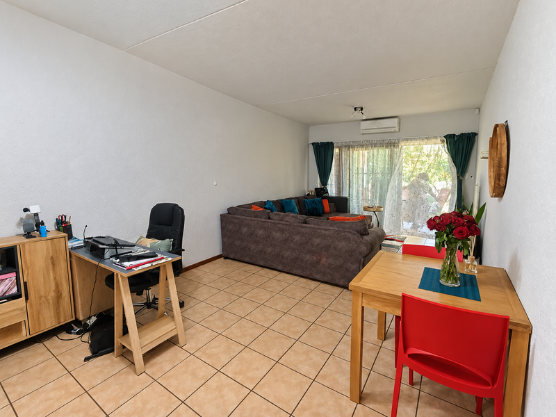 Open plan living and dining area featuring tiled flooring, a wall-mounted air conditioning unit, and sliding glass doors leading to the patio.