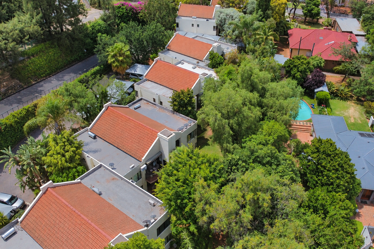 Aerial view of the residential complex featuring multiple units with terracotta tiled roofs, solar geysers, a swimming pool, and established garden surroundings.