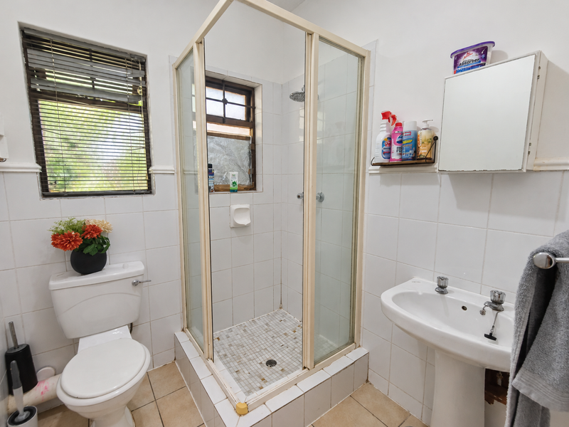 A functional bathroom featuring a pedestal basin, a corner shower cubicle, and a standard toilet with tiled finishes throughout.