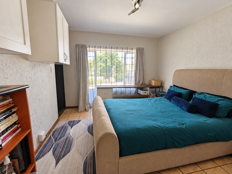 A bedroom featuring textured walls, tiled flooring, and built-in cabinetry, offering a functional space with natural light from the window.