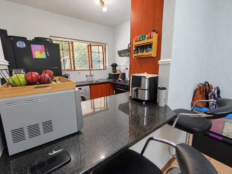 A functional kitchen featuring a granite breakfast bar, built-in cabinetry, stainless steel sink, and integrated hob with extractor fan.
