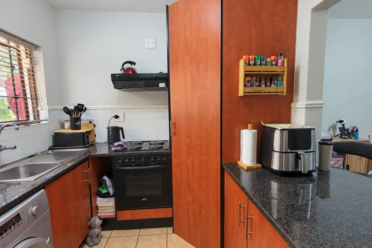 Compact kitchen featuring granite countertops, built-in oven with extractor fan, stainless steel sink, and wood-finish cabinetry with a missing lower cabinet door.