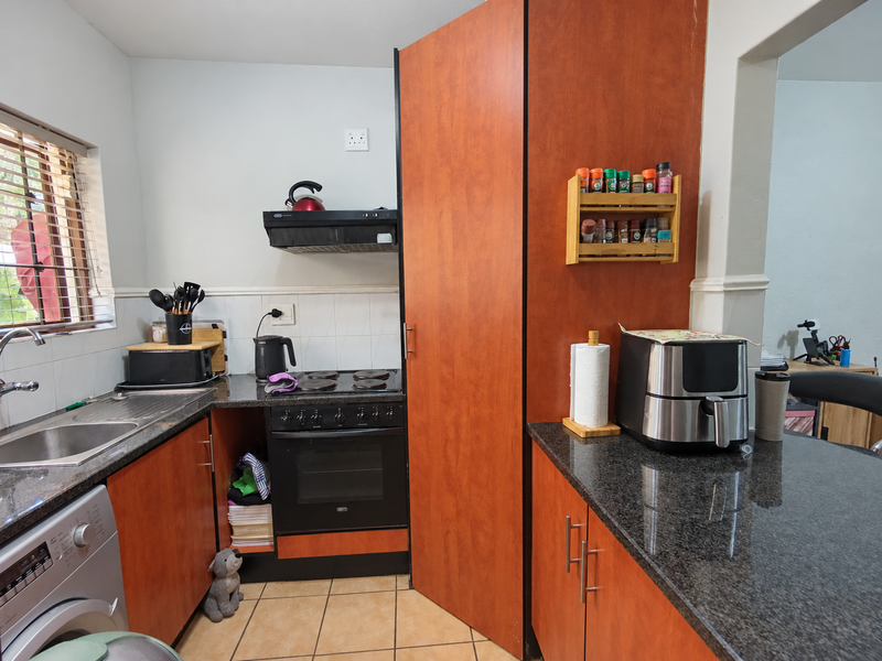 Compact kitchen featuring granite countertops, built-in oven with extractor fan, stainless steel sink, and wood-finish cabinetry with a missing lower cabinet door.
