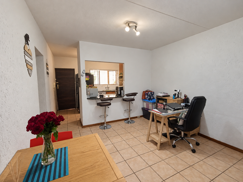 Open plan living area featuring tiled flooring, a breakfast bar with a kitchen pass-through window, and neutral wall finishes.