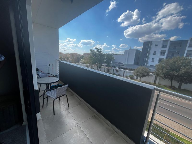 A modern apartment balcony featuring tiled flooring and a sleek stainless steel balustrade with a solid privacy screen, offering an open outdoor view.
