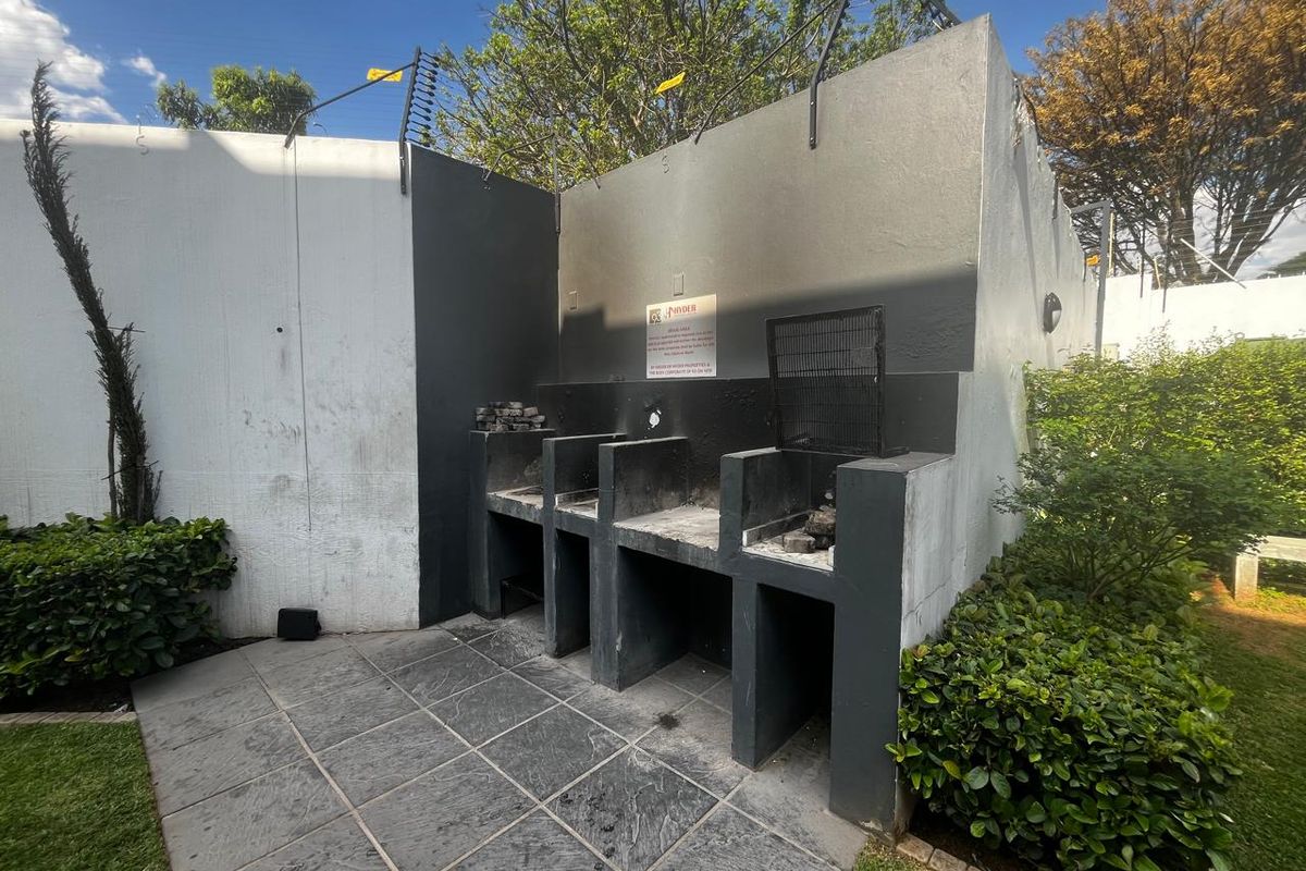Outdoor communal area featuring a built-in braai station with paved flooring and secure boundary walling with electric fencing.