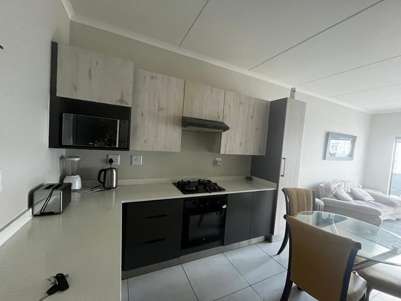 Modern open-plan kitchen featuring sleek two-tone cabinetry, stone countertops, integrated gas hob, oven, and extractor fan, seamlessly flowing into the living and dining area.