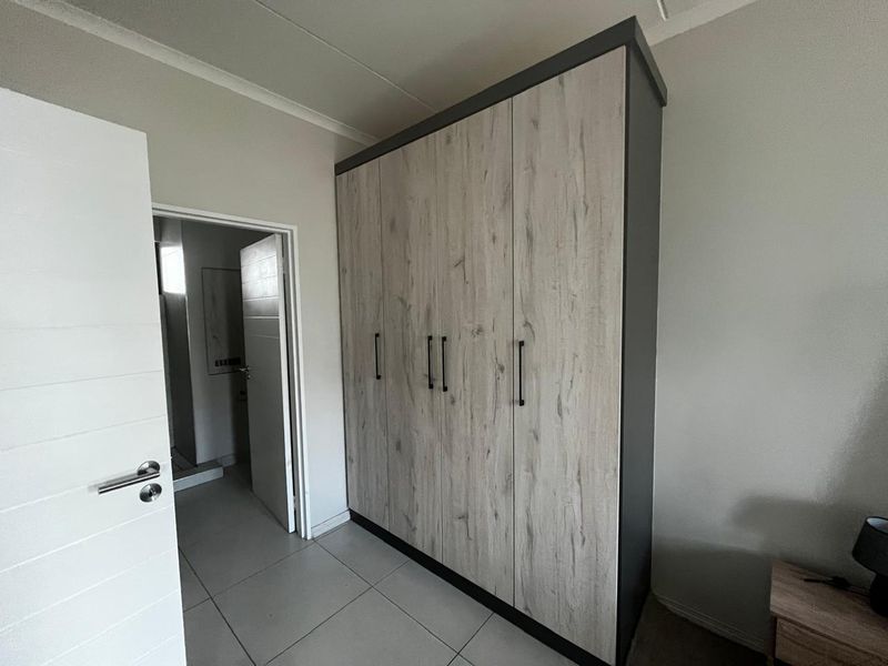 Bedroom featuring a modern built-in wardrobe with wood-grain finish and tiled flooring, leading to an adjacent bathroom.