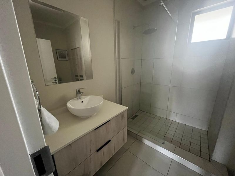 Modern bathroom featuring a vanity with a vessel sink, wall mirror, and a spacious walk-in shower with glass enclosure and tiled finishes.