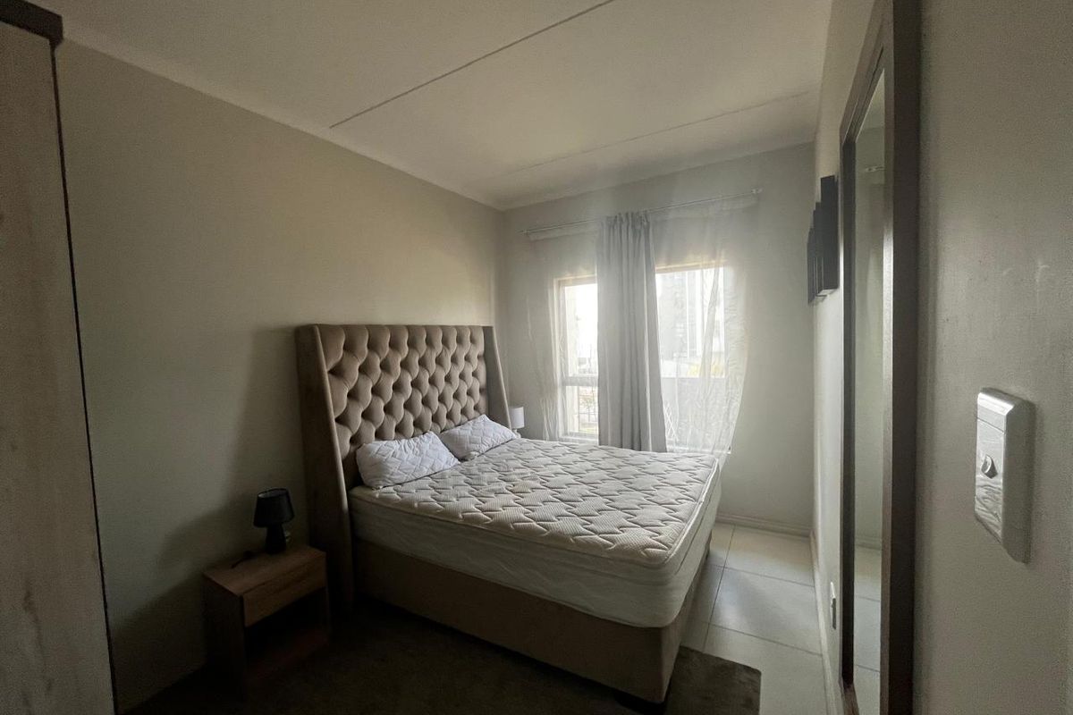 A functional bedroom featuring tiled flooring, a large wall-mounted mirror, and natural light from the window.