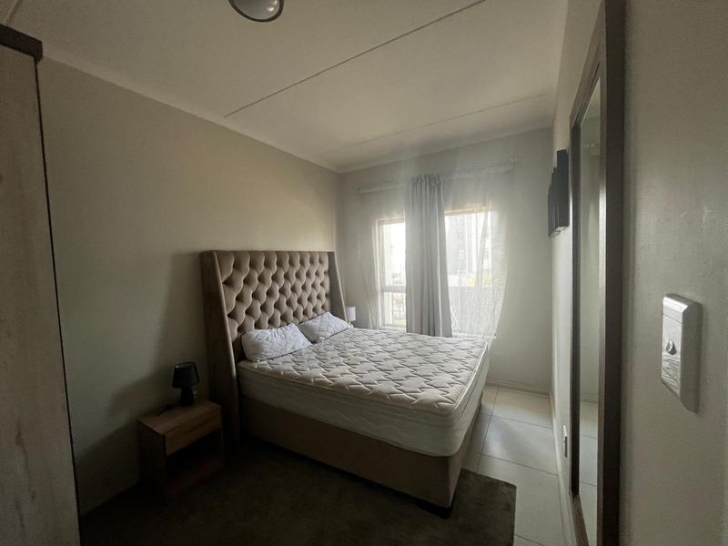 A functional bedroom featuring tiled flooring, a large wall-mounted mirror, and natural light from the window.