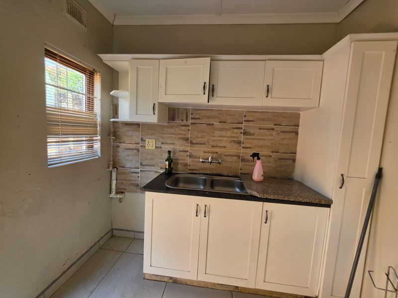 A functional scullery area featuring built-in white cabinetry, a double basin sink, tiled splashback, and tiled flooring, offering practical utility space.