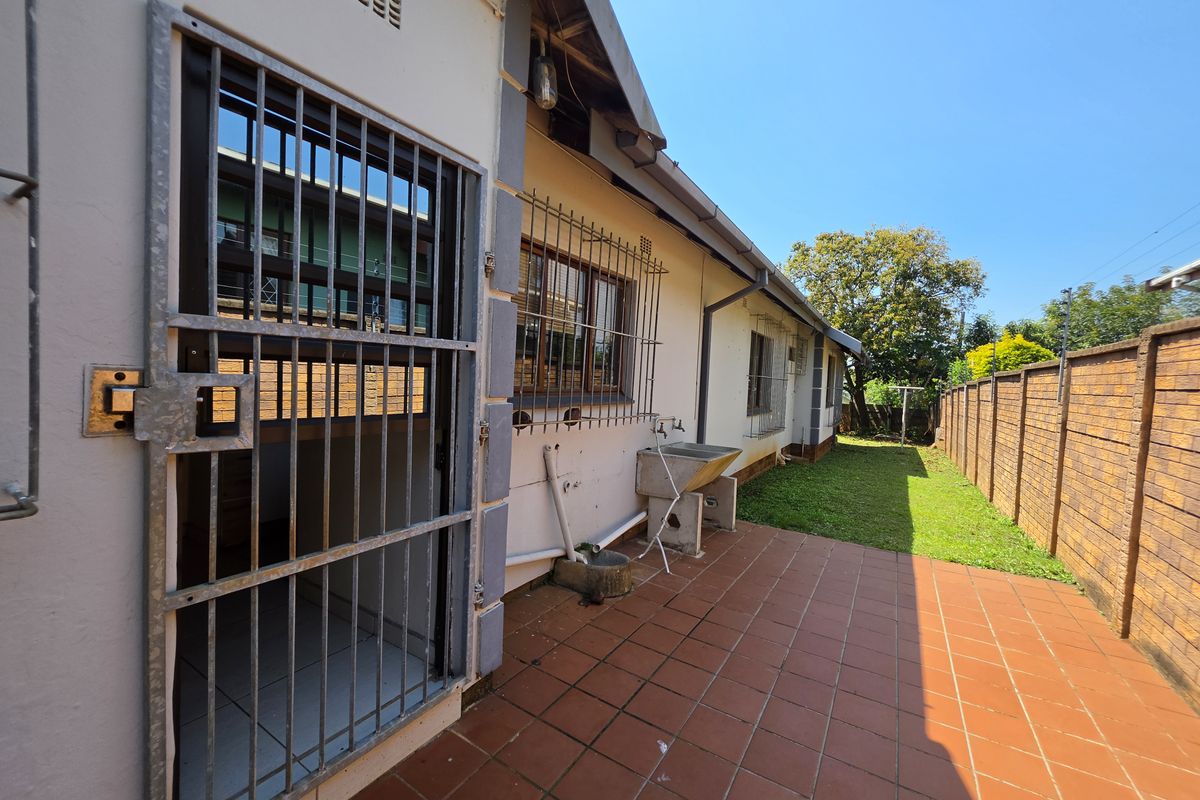 Rear exterior view featuring a tiled patio, security gate, external utility sink, and a brick boundary wall with a small grassed area.