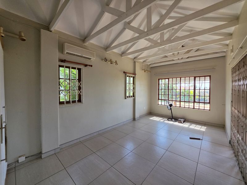 Spacious living area featuring exposed white timber roof trusses, tiled flooring, and split-system air conditioning, offering a bright and versatile space.
