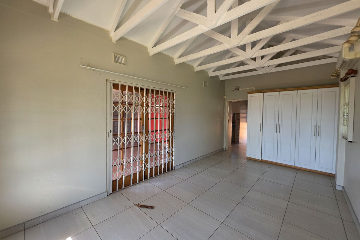 Spacious bedroom featuring exposed white roof trusses, tiled flooring, and extensive built-in cupboard storage with a secure sliding gate entrance.