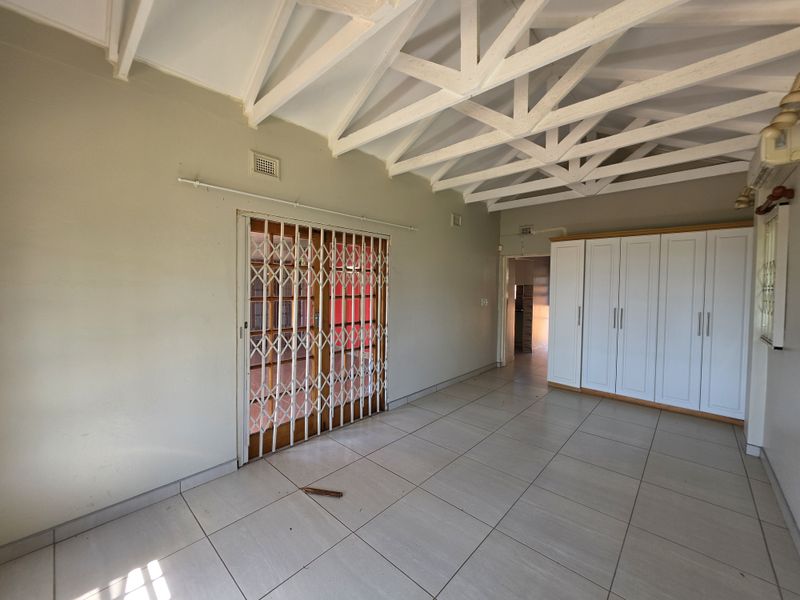 Spacious bedroom featuring exposed white roof trusses, tiled flooring, and extensive built-in cupboard storage with a secure sliding gate entrance.