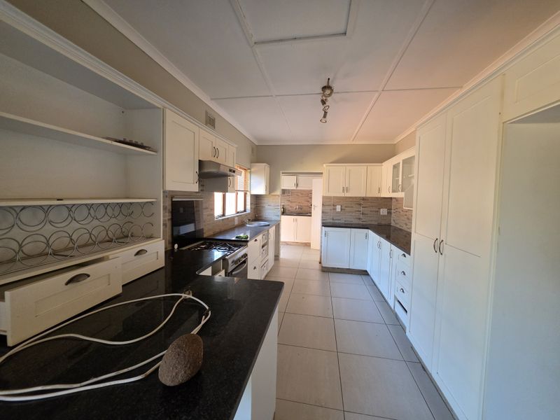 Spacious kitchen featuring white cabinetry, dark granite countertops, gas hob, extractor fan, and tiled flooring, with an adjacent scullery area.