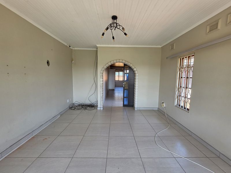 An empty living room featuring tiled flooring, an arched doorway, and a window with a security gate, requiring minor cosmetic updates.