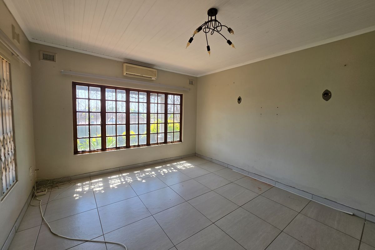 A vacant living room featuring tiled flooring, a timber-framed window, and a wall-mounted air conditioning unit, offering a blank canvas for personalization.