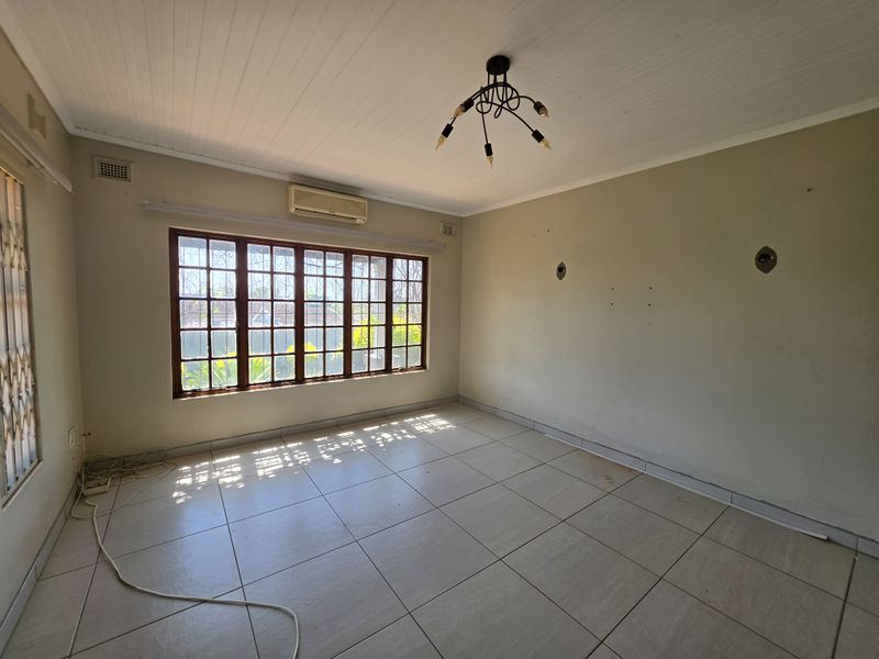 A vacant living room featuring tiled flooring, a timber-framed window, and a wall-mounted air conditioning unit, offering a blank canvas for personalization.
