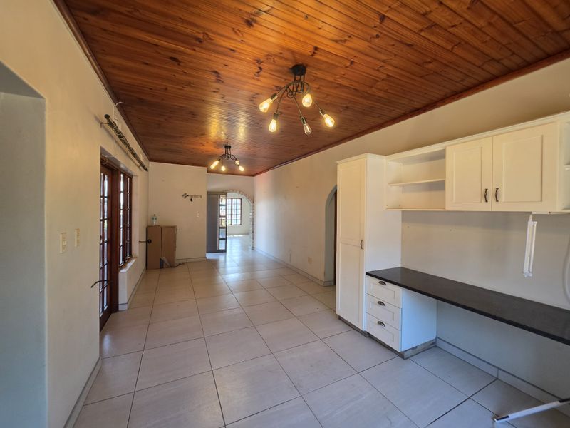 Spacious open-plan area featuring a warm timber ceiling, tiled flooring, and built-in cabinetry with a dark countertop, offering a versatile layout.