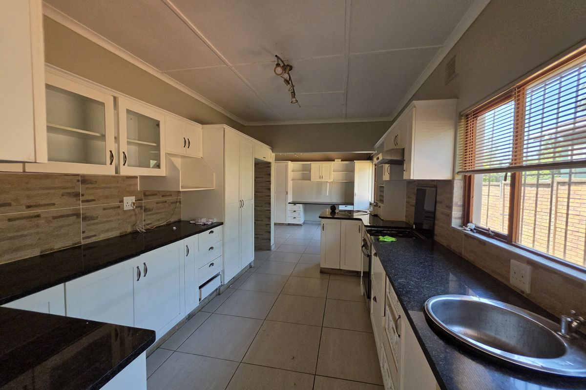 Spacious kitchen featuring white cabinetry, dark granite countertops, tiled flooring, and a functional layout with a separate scullery area.