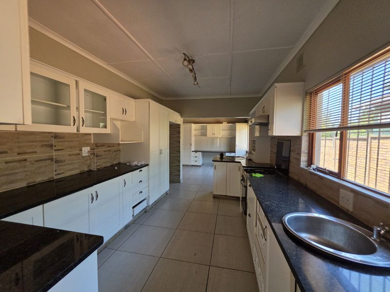 Spacious kitchen featuring white cabinetry, dark granite countertops, tiled flooring, and a functional layout with a separate scullery area.