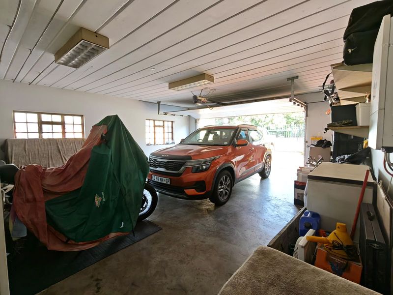 A functional double garage featuring concrete flooring, timber panel ceilings, and steel-framed windows, providing ample space for vehicle storage.