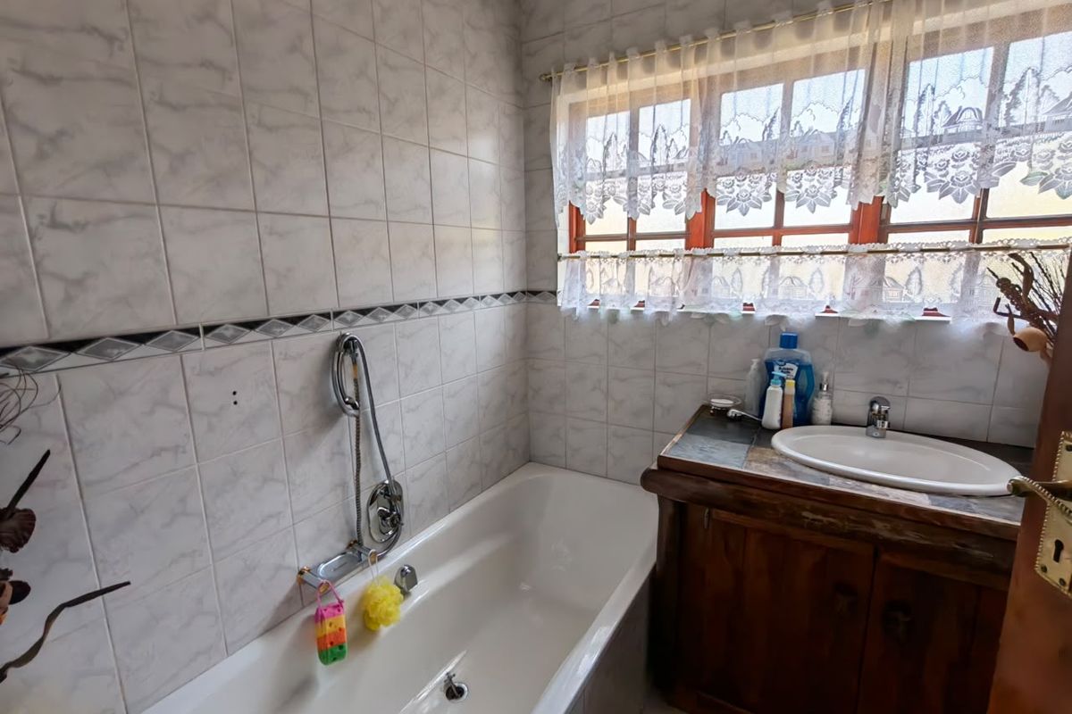 A functional bathroom featuring a built-in vanity with a ceramic basin, a bathtub with a handheld shower mixer, and full-height wall tiling.