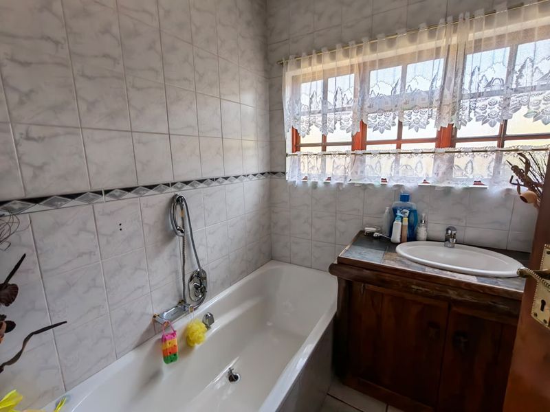 A functional bathroom featuring a built-in vanity with a ceramic basin, a bathtub with a handheld shower mixer, and full-height wall tiling.