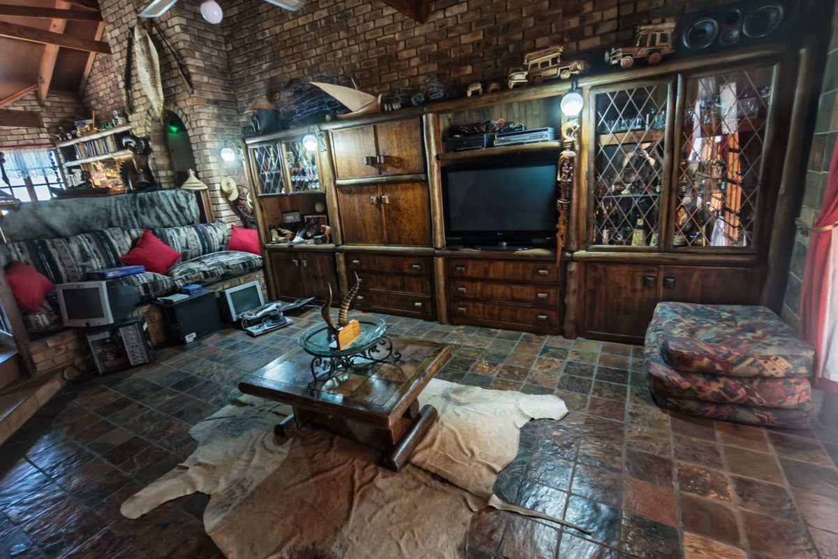 Spacious living room featuring a rustic brick wall, exposed timber ceiling beams, slate tile flooring, and extensive built-in wooden cabinetry.