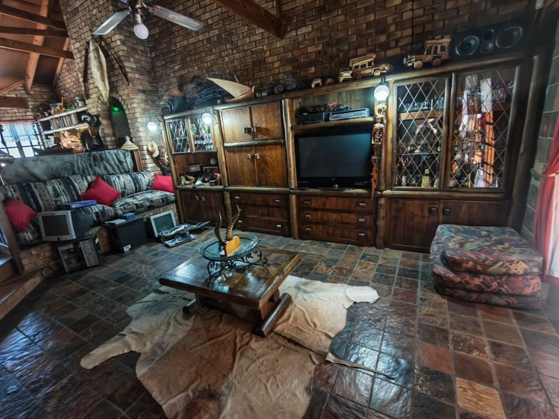 Spacious living room featuring a rustic brick wall, exposed timber ceiling beams, slate tile flooring, and extensive built-in wooden cabinetry.