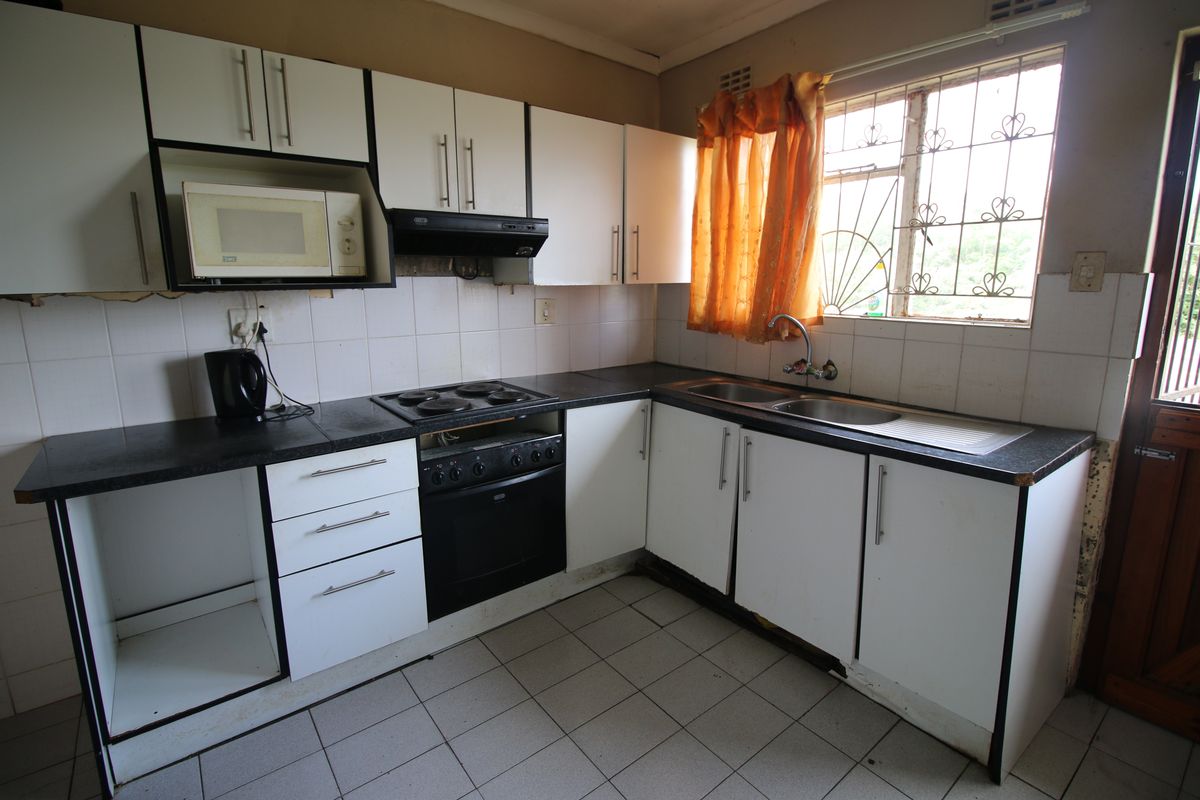 A functional kitchen featuring built-in cabinetry, an electric stove with oven, extractor fan, and a double sink with tiled backsplash and flooring.