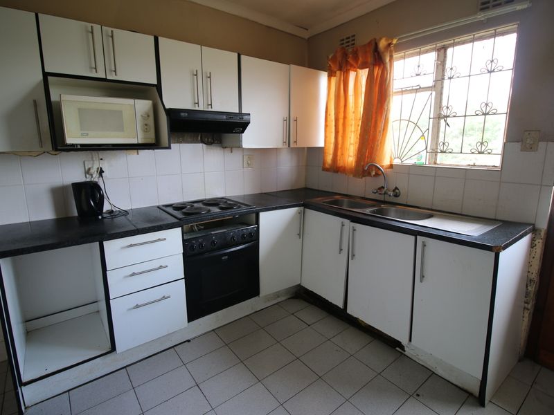 A functional kitchen featuring built-in cabinetry, an electric stove with oven, extractor fan, and a double sink with tiled backsplash and flooring.