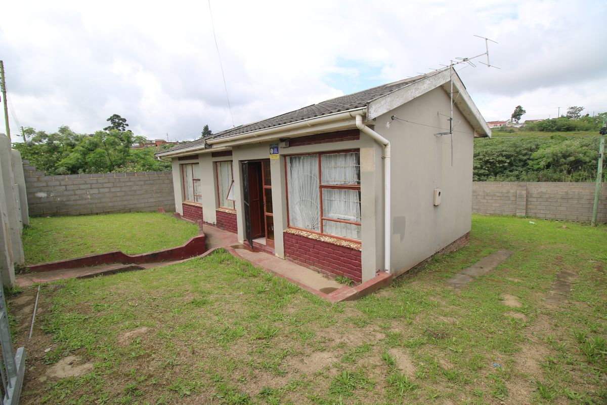 Rear view of a detached house featuring a concrete tile roof, brick perimeter wall, and surrounding lawn area.