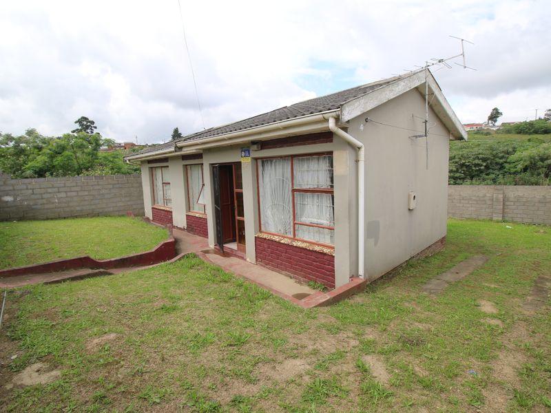 Rear view of a detached house featuring a concrete tile roof, brick perimeter wall, and surrounding lawn area.