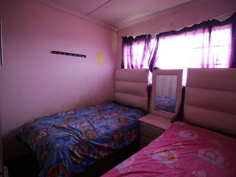 A bedroom featuring built-in headboards and a bedside table, requiring cosmetic updates to the wall finishes.