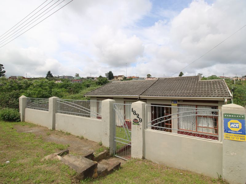 Front view of a single-story house featuring a tiled roof, secure metal gate, and a concrete boundary wall with security fencing.