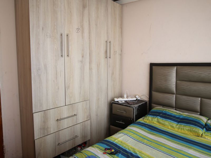 A bedroom featuring a light wood-grain built-in wardrobe with integrated drawers and metal handles.