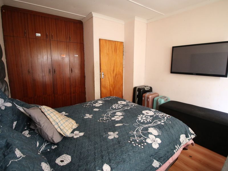 A bedroom featuring laminate flooring, built-in wooden cupboards, and coving detail, offering a functional space with potential for cosmetic updates.