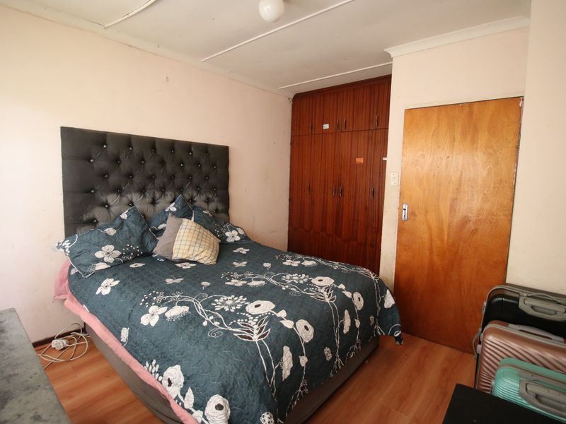 A bedroom featuring built-in wooden wardrobes, laminate flooring, and a coved ceiling. The room requires cosmetic updates to improve its overall condition.