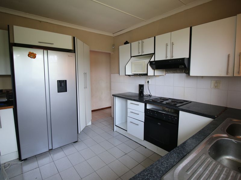 A functional kitchen featuring white cabinetry, dark laminate countertops, an integrated oven and hob, and tiled flooring, requiring some cosmetic updates.