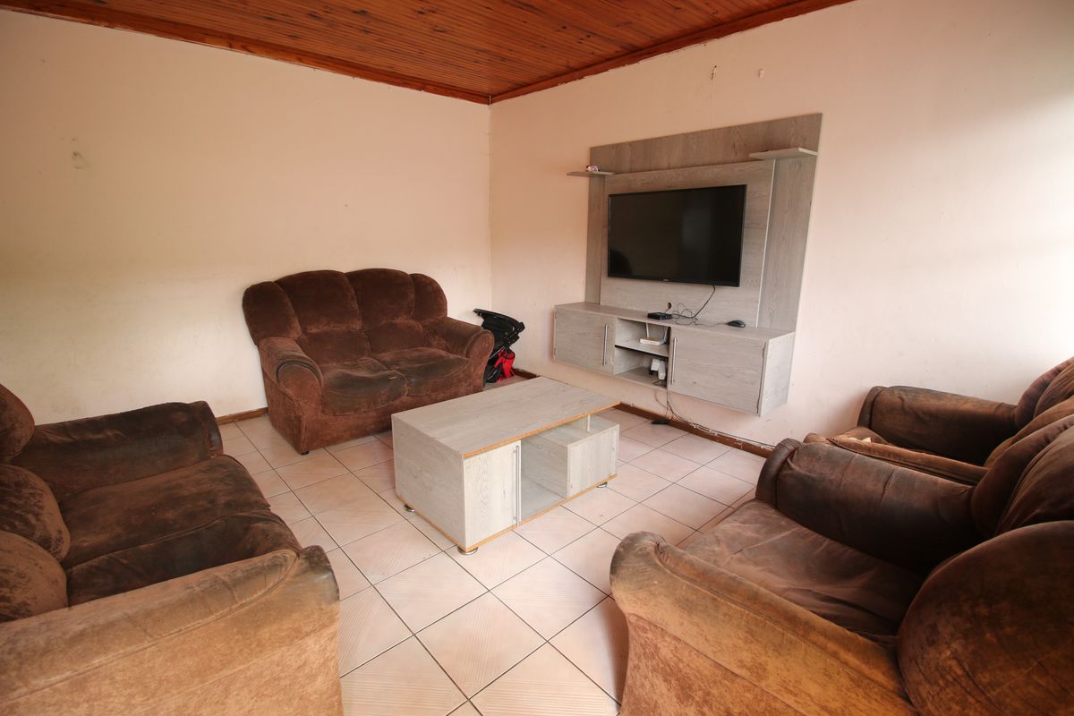 A living room featuring tiled flooring, a timber ceiling, and a built-in media unit, offering a functional space with potential for cosmetic updates.
