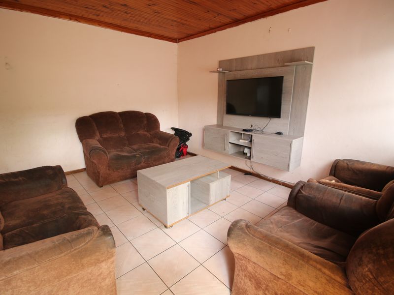 A living room featuring tiled flooring, a timber ceiling, and a built-in media unit, offering a functional space with potential for cosmetic updates.