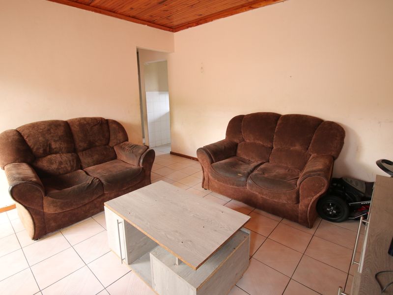 A living room featuring tiled flooring and a timber tongue and groove ceiling, providing a functional space with direct access to an adjacent room.